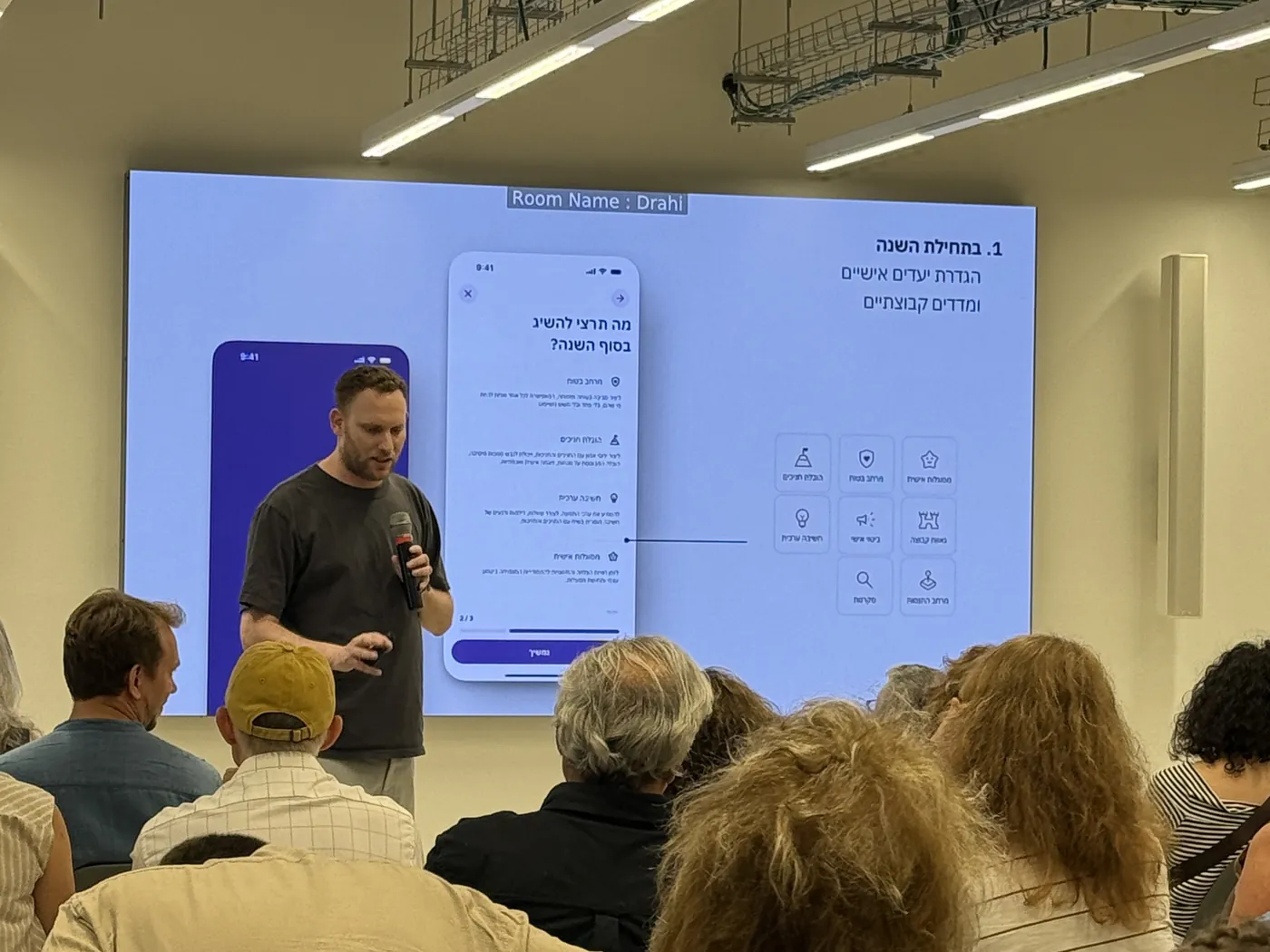 Aviv presenting Baloop to an audience at Bezalel, with the app's screens on a large display behind him
